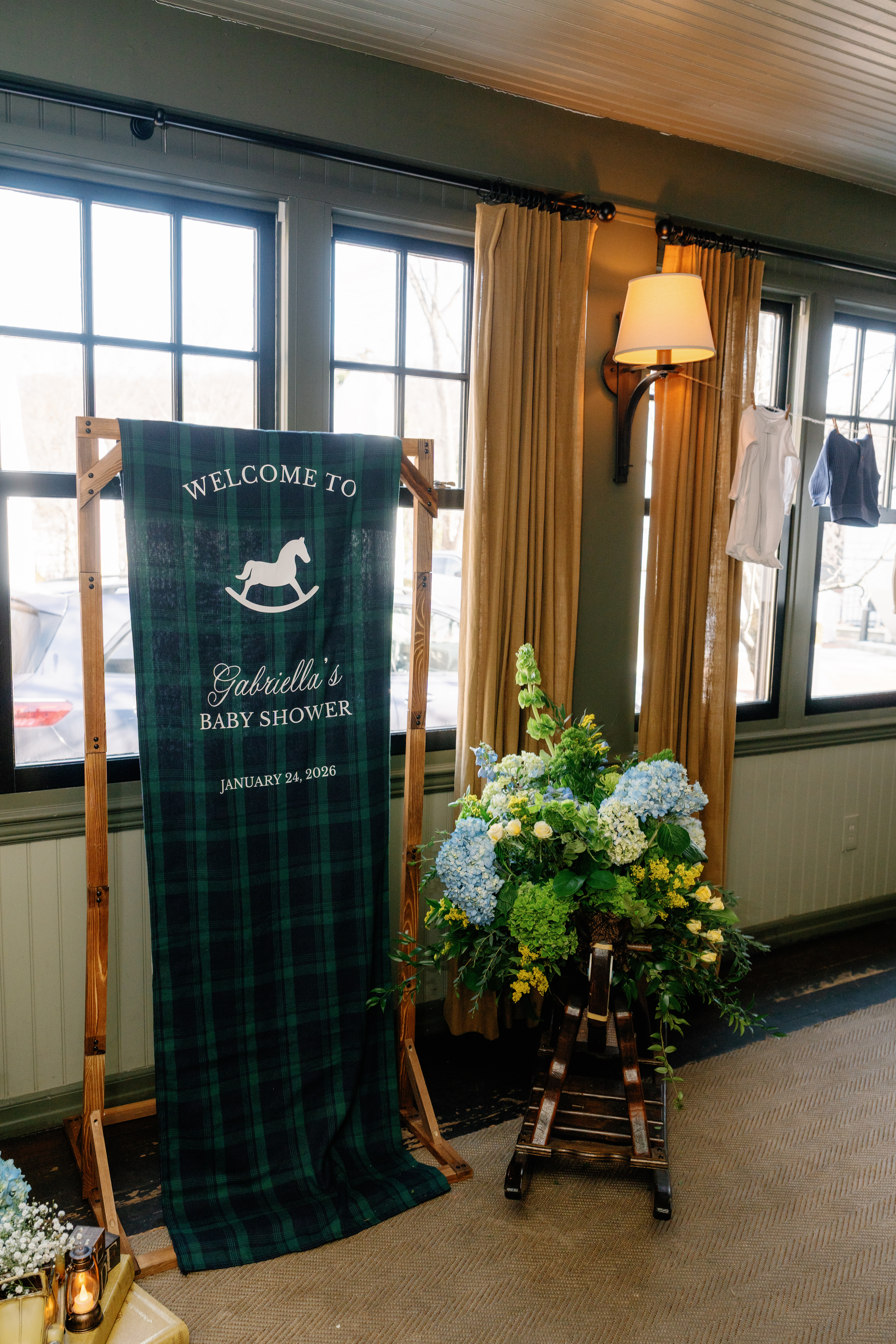 Handmade plaid welcome banner with rocking horse motif and blue hydrangea arrangement for a baby shower