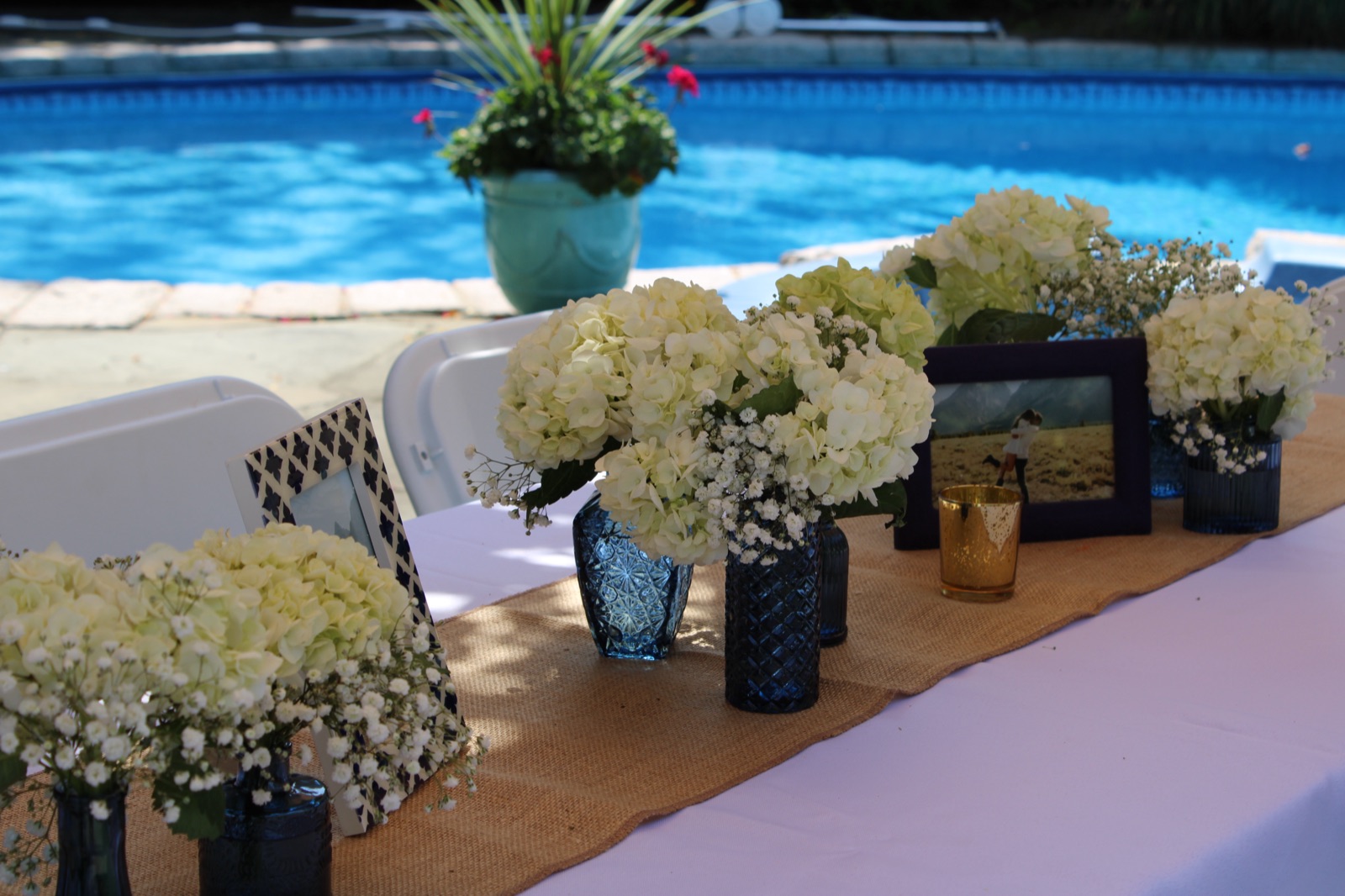 Poolside party table with white hydrangeas in navy blue vases and burlap runner